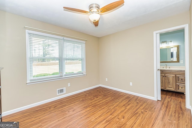 unfurnished bedroom featuring wood-type flooring, connected bathroom, ceiling fan, and sink