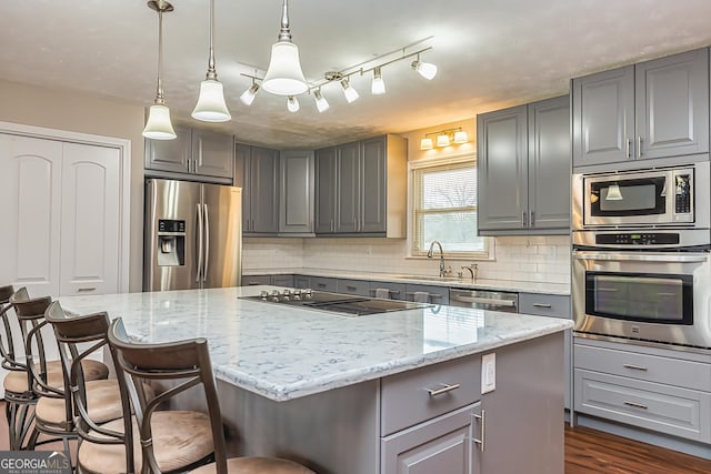 kitchen featuring a center island, sink, hanging light fixtures, stainless steel appliances, and light stone counters