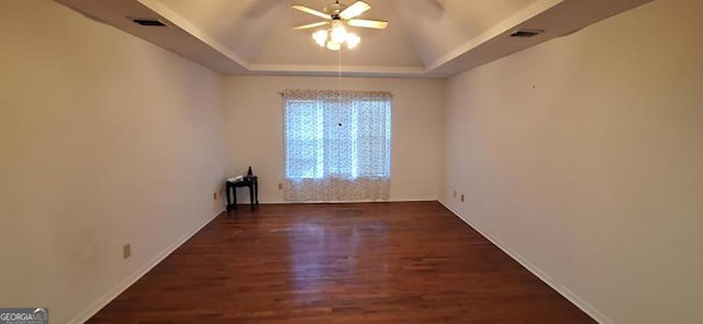 empty room with dark hardwood / wood-style floors, a raised ceiling, and ceiling fan