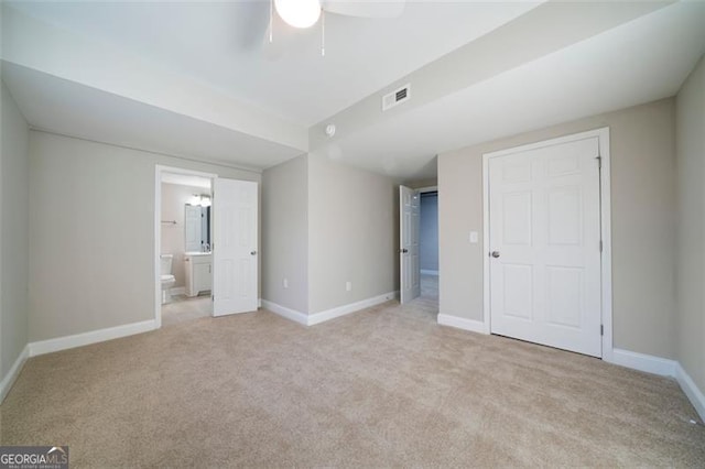 unfurnished bedroom featuring ceiling fan, light colored carpet, and ensuite bath