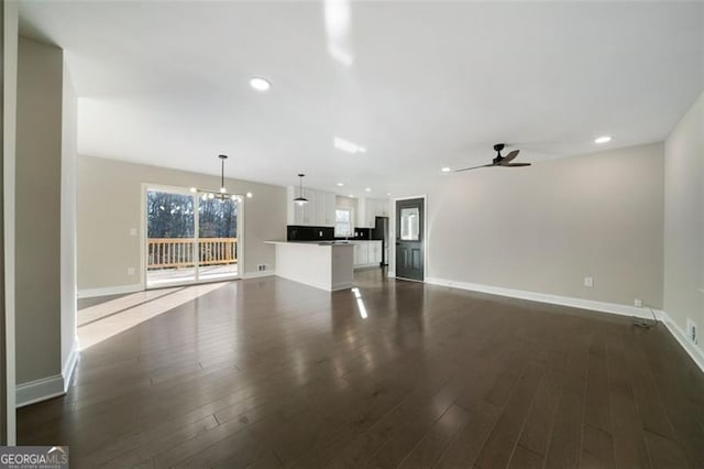 unfurnished living room featuring ceiling fan with notable chandelier and dark wood-type flooring