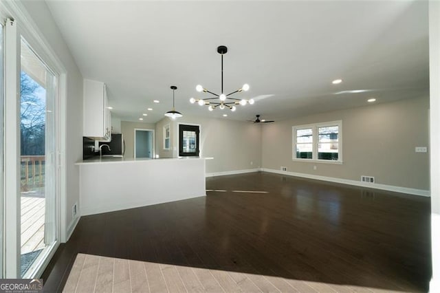 unfurnished living room with dark hardwood / wood-style flooring, ceiling fan with notable chandelier, and sink