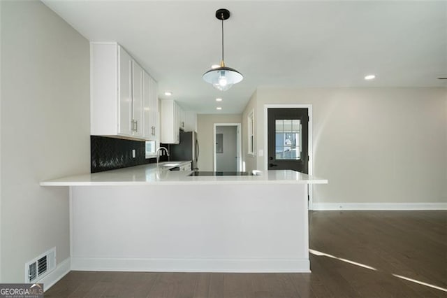 kitchen featuring hanging light fixtures, dark hardwood / wood-style flooring, kitchen peninsula, decorative backsplash, and white cabinets