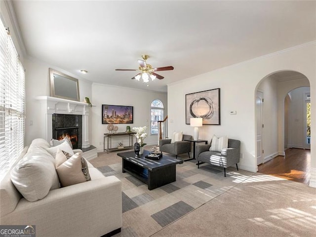 carpeted living room featuring a tiled fireplace, crown molding, and ceiling fan