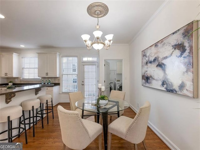 dining area featuring washing machine and dryer, dark hardwood / wood-style floors, an inviting chandelier, and ornamental molding