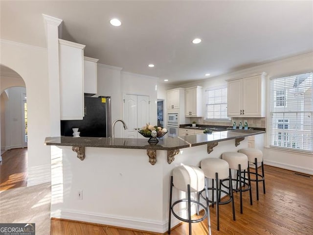 kitchen featuring white cabinetry, a breakfast bar area, stainless steel refrigerator, and ornamental molding