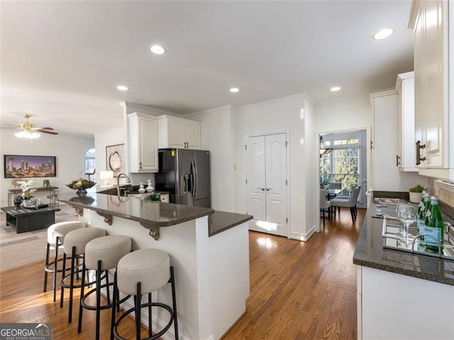 kitchen with kitchen peninsula, stainless steel fridge with ice dispenser, ceiling fan, a kitchen bar, and white cabinetry