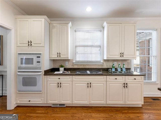 kitchen featuring white cabinetry, dark wood-type flooring, tasteful backsplash, white appliances, and ornamental molding