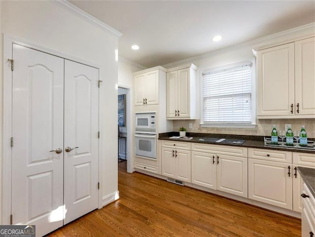 kitchen with white cabinetry, tasteful backsplash, dark hardwood / wood-style flooring, crown molding, and white appliances