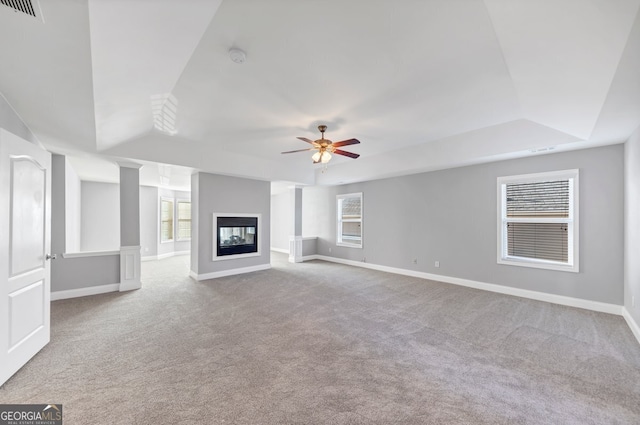 unfurnished living room featuring a multi sided fireplace, light carpet, a tray ceiling, and ceiling fan