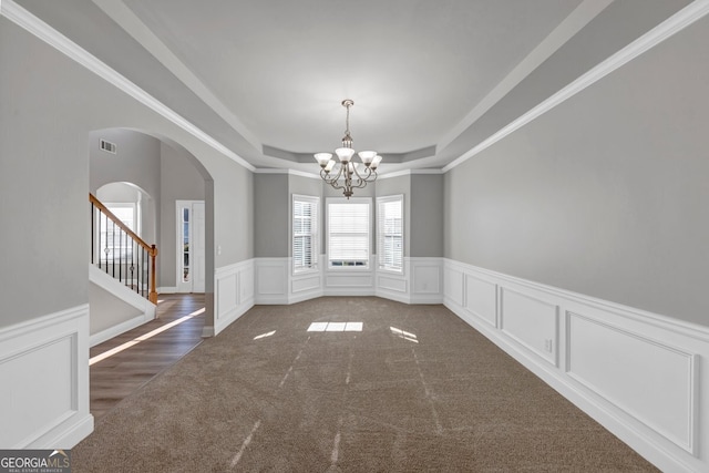 carpeted spare room with a tray ceiling, crown molding, and a notable chandelier