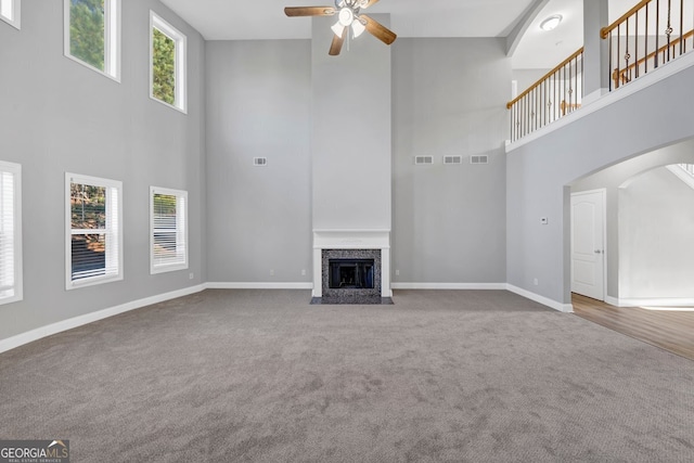 unfurnished living room with carpet flooring, ceiling fan, and a high ceiling