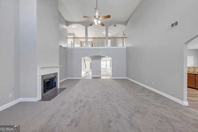 unfurnished living room with ceiling fan, sink, light carpet, and a high ceiling