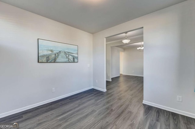 empty room with a notable chandelier and dark hardwood / wood-style flooring