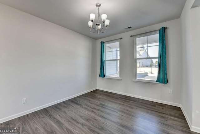 spare room with dark hardwood / wood-style flooring and an inviting chandelier