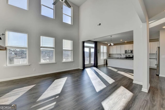 unfurnished living room featuring ceiling fan with notable chandelier, dark hardwood / wood-style flooring, a towering ceiling, and sink