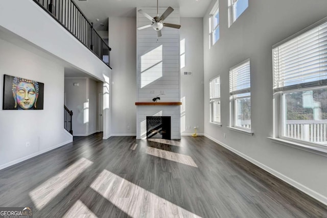 unfurnished living room featuring ceiling fan, a large fireplace, a towering ceiling, and dark wood-type flooring