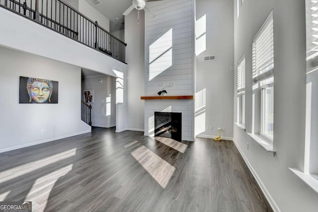 unfurnished living room featuring a fireplace, a high ceiling, dark hardwood / wood-style floors, and ceiling fan