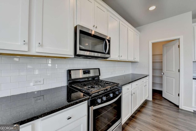 kitchen with decorative backsplash, dark stone countertops, light wood-type flooring, white cabinetry, and stainless steel appliances