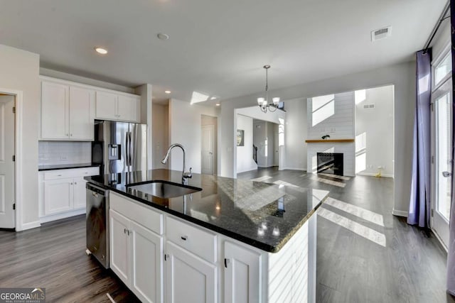 kitchen featuring a brick fireplace, stainless steel appliances, a kitchen island with sink, sink, and white cabinetry