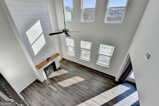 unfurnished living room with ceiling fan, a large fireplace, and dark hardwood / wood-style flooring