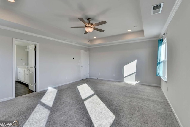 unfurnished room with dark colored carpet, ceiling fan, crown molding, and a tray ceiling