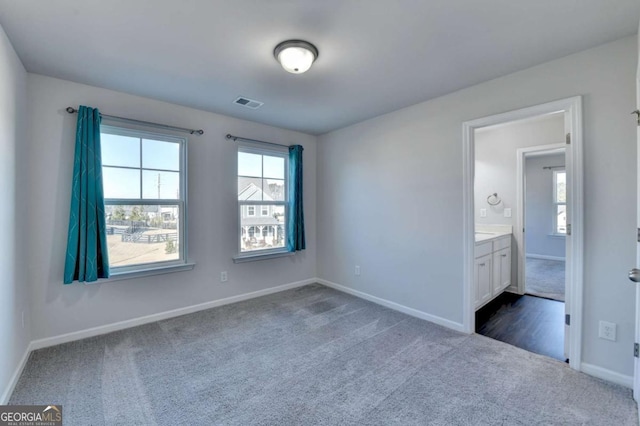 unfurnished bedroom featuring connected bathroom and dark colored carpet