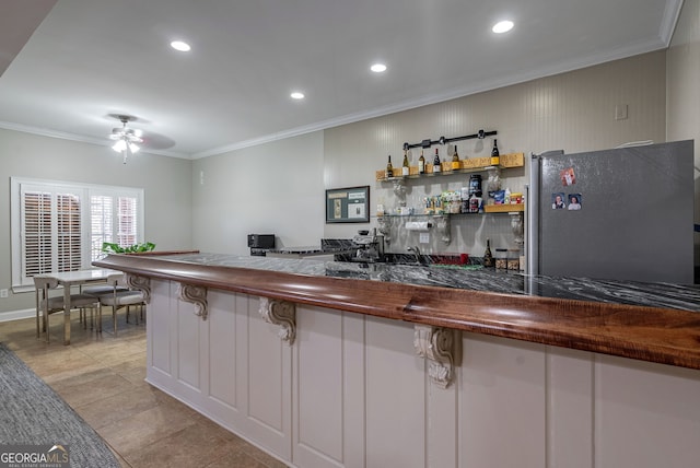 kitchen with wood counters, white cabinetry, ornamental molding, and stainless steel refrigerator