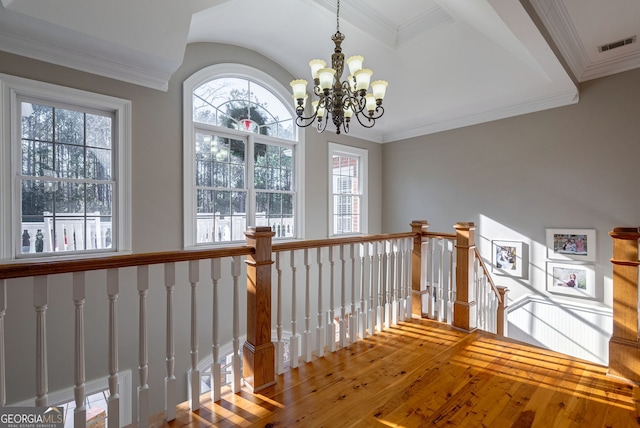 hallway with hardwood / wood-style floors, lofted ceiling, ornamental molding, and an inviting chandelier