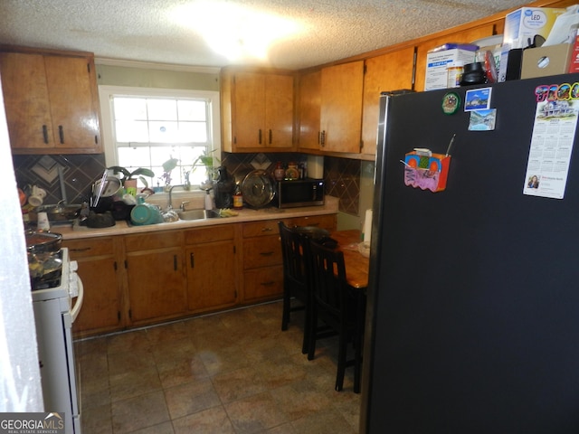 kitchen with a textured ceiling, white gas stove, backsplash, and fridge