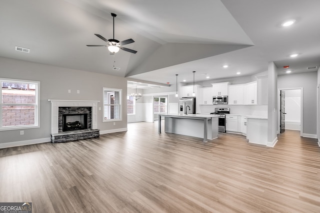 unfurnished living room with ceiling fan with notable chandelier, a stone fireplace, light hardwood / wood-style floors, and vaulted ceiling