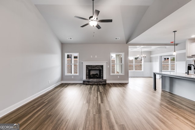 unfurnished living room featuring a stone fireplace, ceiling fan with notable chandelier, and hardwood / wood-style flooring