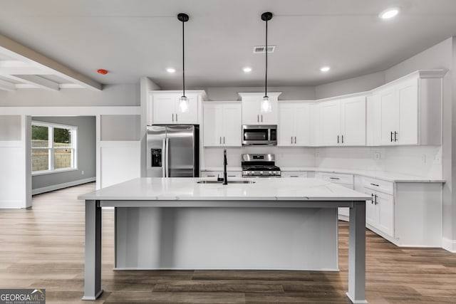 kitchen featuring sink, appliances with stainless steel finishes, white cabinetry, hanging light fixtures, and an island with sink