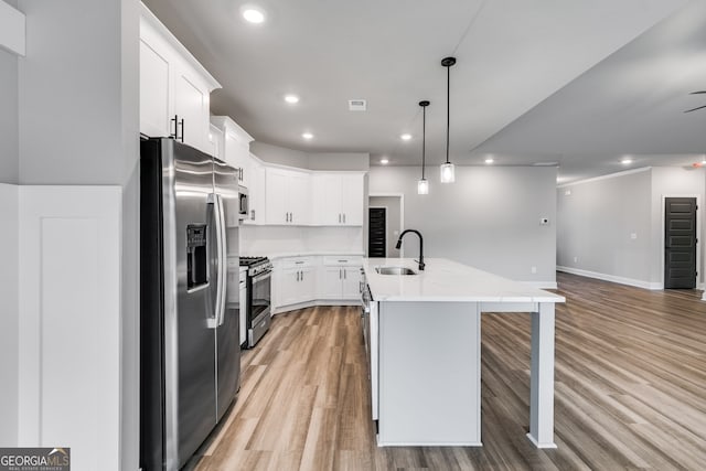 kitchen with sink, appliances with stainless steel finishes, white cabinetry, a kitchen island with sink, and decorative light fixtures