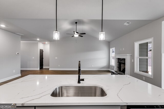 kitchen with a kitchen island with sink, decorative light fixtures, a fireplace, and light stone countertops