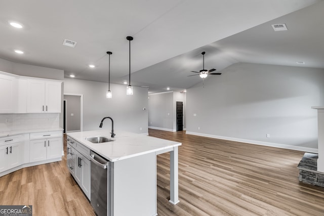 kitchen featuring an island with sink, sink, white cabinets, and light stone counters