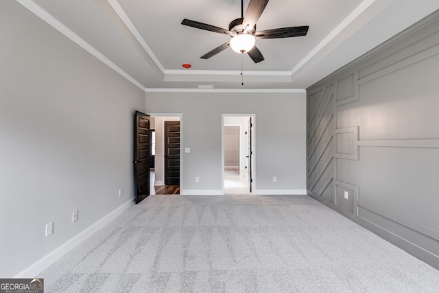 unfurnished bedroom featuring crown molding, a raised ceiling, light carpet, a spacious closet, and a closet