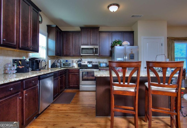 kitchen featuring sink, decorative backsplash, light wood-type flooring, light stone counters, and stainless steel appliances