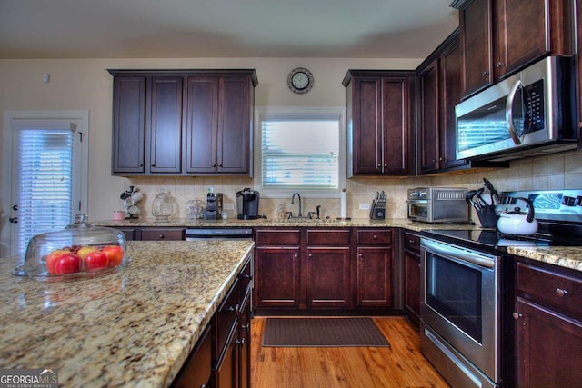 kitchen featuring sink, light wood-type flooring, light stone countertops, tasteful backsplash, and stainless steel appliances