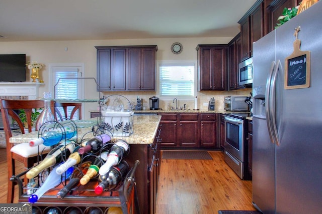 kitchen featuring sink, light stone counters, light hardwood / wood-style floors, decorative backsplash, and appliances with stainless steel finishes