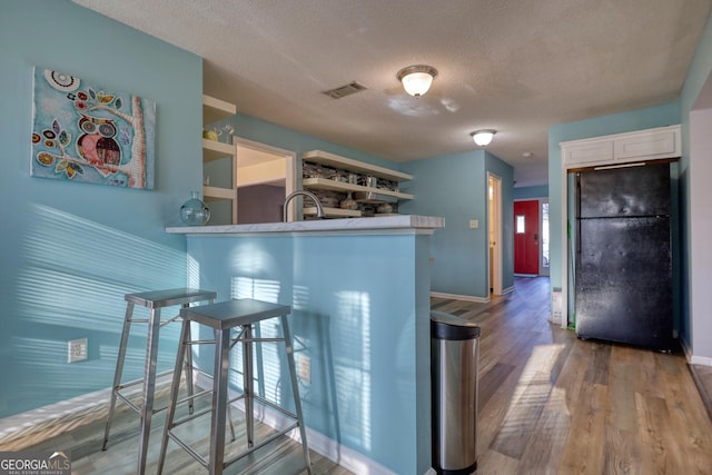 kitchen with kitchen peninsula, a textured ceiling, black fridge, hardwood / wood-style floors, and white cabinetry