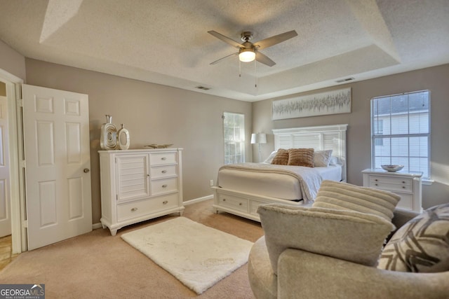 bedroom with ceiling fan, multiple windows, a textured ceiling, and a tray ceiling