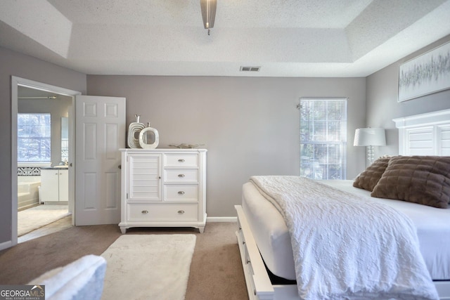 carpeted bedroom featuring ensuite bathroom, a raised ceiling, and a textured ceiling