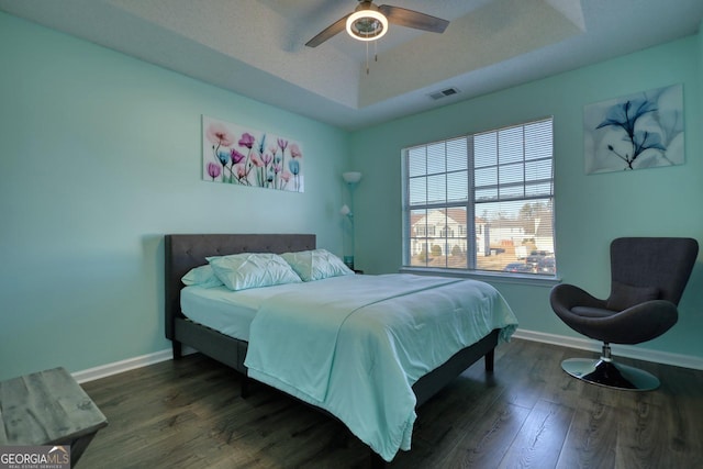 bedroom with dark hardwood / wood-style flooring, a raised ceiling, and ceiling fan