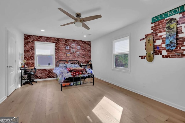 bedroom featuring ceiling fan, light hardwood / wood-style floors, and brick wall