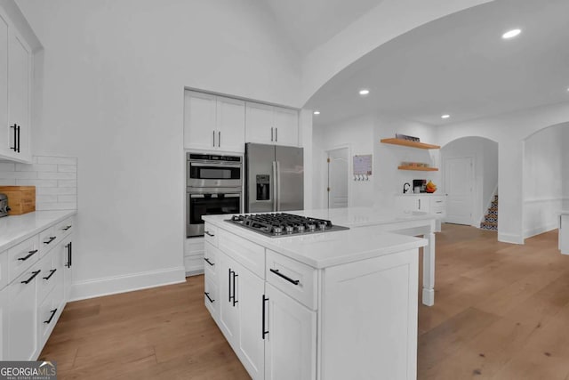 kitchen with white cabinets, appliances with stainless steel finishes, a kitchen island, tasteful backsplash, and light wood-type flooring