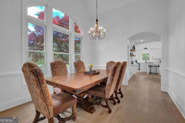 dining space featuring high vaulted ceiling, light wood-type flooring, and an inviting chandelier