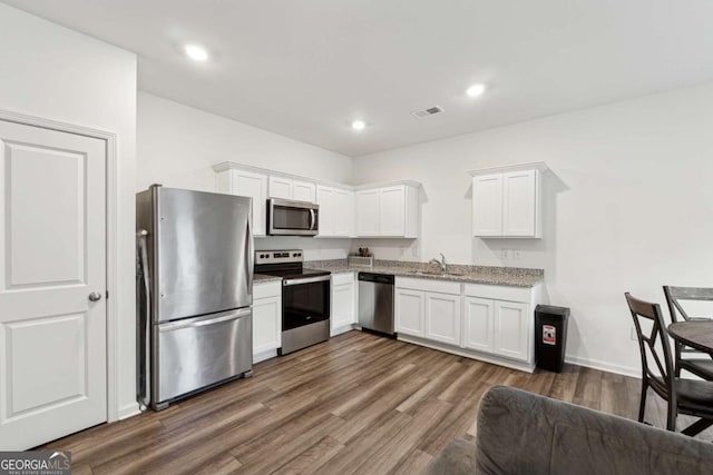 kitchen with light stone countertops, sink, dark hardwood / wood-style floors, white cabinets, and appliances with stainless steel finishes