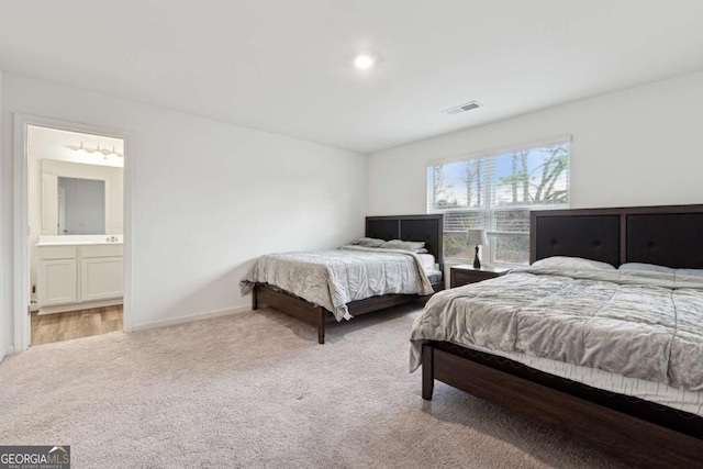 bedroom with ensuite bathroom and light carpet