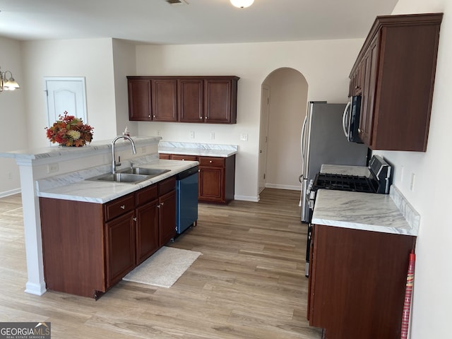 kitchen with arched walkways, stainless steel appliances, a sink, light countertops, and light wood-type flooring